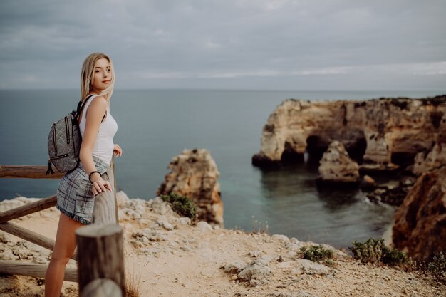 Jonge schoonheid blonde vrouw reiziger kijken naar de zee en de klif op het mooie strand van Portugal.