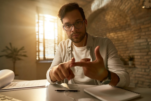 Gratis foto jonge serieuze ondernemer die instructies geeft en gebaren maakt terwijl hij naar de camera op kantoor kijkt