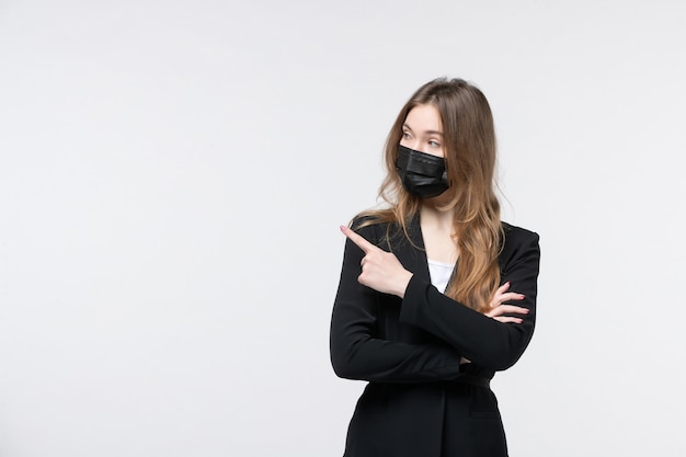 Jonge serieuze zakenvrouw in pak met een medisch masker en iemand aan de rechterkant wijzend op een geïsoleerde witte muur