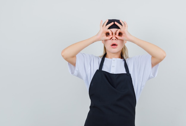 Jonge serveerster die glazengebaar in uniform en schort toont