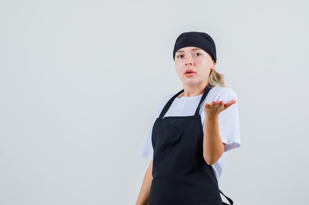 Jonge serveerster die palm op vragende wijze in uniform en schort opheft