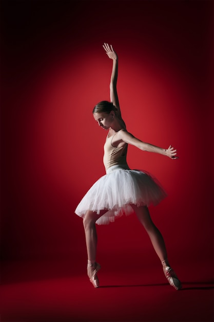 Jonge sierlijke vrouwelijke balletdanser of klassieke ballerina dansen op rode studio.