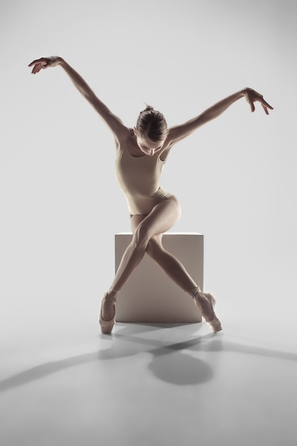 Jonge sierlijke vrouwelijke balletdanser of klassieke ballerina dansen op witte studio.