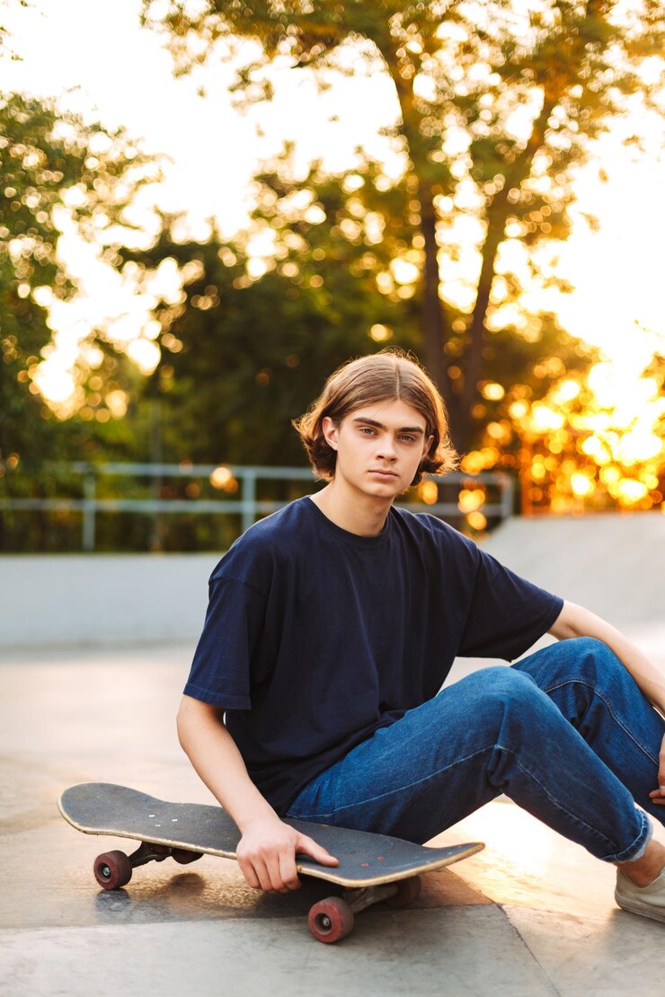 Gratis Foto jonge skater in zwarte t-shirt en spijkerbroek die zorgvuldig in de camera kijkt met skateboard die tijd doorbrengt in het moderne skatepark