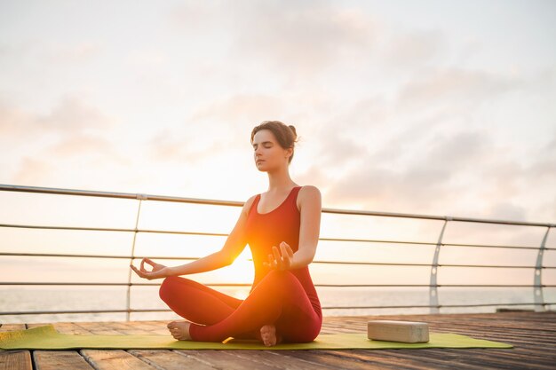 Jonge slanke mooie aantrekkelijke vrouw doet yoga in de ochtend op zonsopgang over zee, gezonde levensstijl