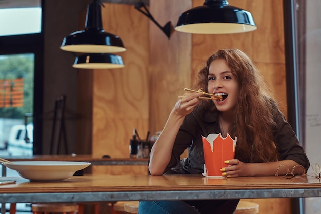 Jonge slimme curly studente zittend aan een tafel in de kantine van de universiteit tijdens een pauze.