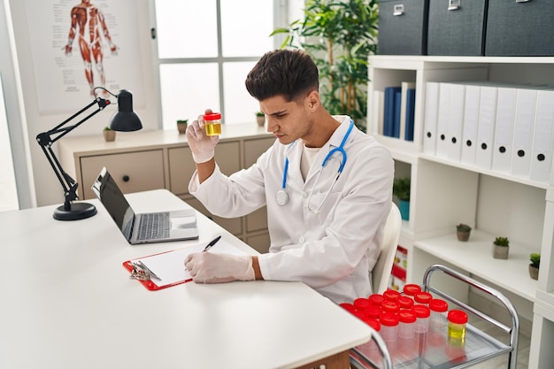 Jonge spaanse man met doktersuniform die urinereageerbuis analyseert in de kliniek