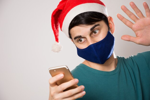 Jonge Spaanse man met een gezichtsmasker en een kerstmuts groet tijdens een videogesprek