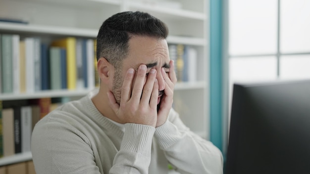 Jonge spaanse man student met behulp van computer gestrest aan de universiteit van de bibliotheek