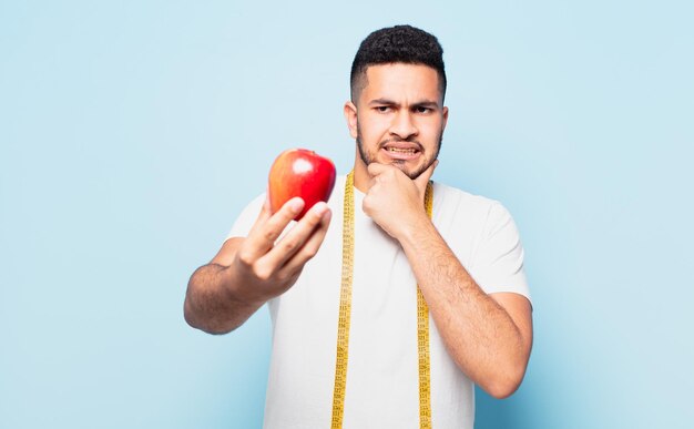 Jonge spaanse man twijfelt of onzekere uitdrukking en houdt een appel vast. dieet concept