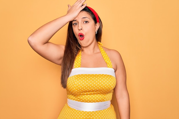 Gratis foto jonge spaanse pin-up vrouw dragen mode sexy jaren 50 stijl over gele achtergrond verrast met de hand op het hoofd voor fout onthoud fout slecht geheugen concept vergeten