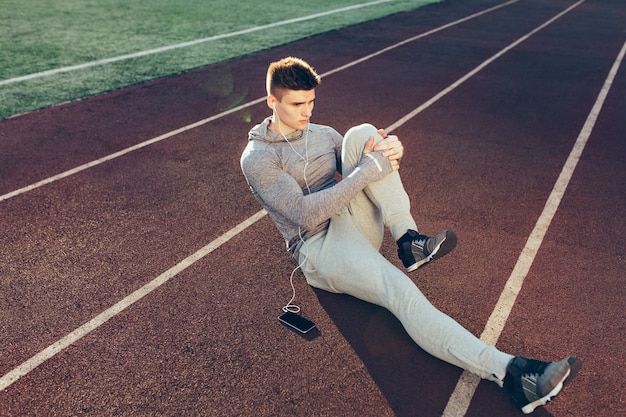 Jonge sportieve kerel bij training op het goede spoor in de ochtend op stadion. Hij draagt een grijs sportpak. Uitzicht van boven.