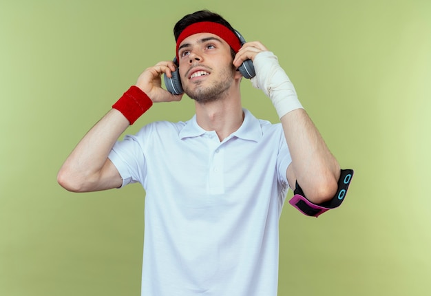 Gratis foto jonge sportieve man in hoofdband met koptelefoon en smartphone armband blij en positief genieten van zijn muziek over groen