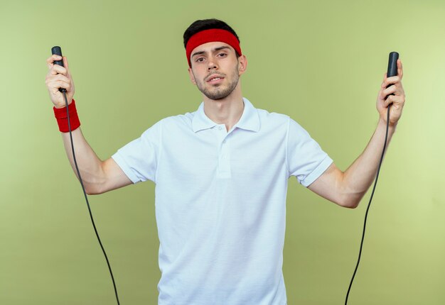 Jonge sportieve man in hoofdband met springtouw op zoek moe en uitgeput over groen