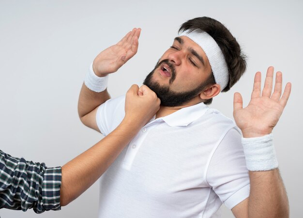 Jonge sportieve man met hoofdband en polsband geslagen door iemand die handen opheft