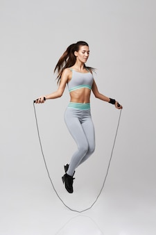 Jonge sportieve vrouw die oefeningen met touwtjespringen op wit doen.