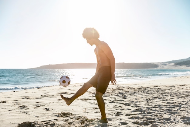 Gratis foto jonge sportman die bal op zeekust werpt