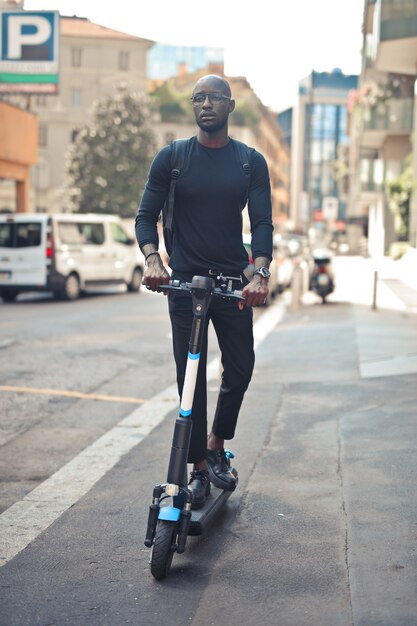 Jonge stijlvolle Afrikaanse man met bril die overdag op een scooter rijdt onder het zonlicht