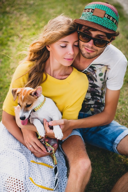 Jonge stijlvolle hipster paar verliefd zittend op gras spelen hond in tropisch strand