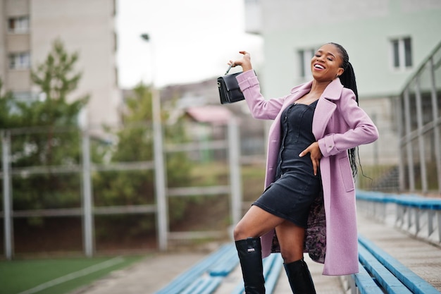 Jonge, stijlvolle, mooie afro-amerikaanse vrouw in de straat bij de tribunes van het stadion met een mode-outfitjas met handtas