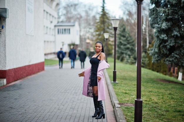 Jonge, stijlvolle, mooie Afro-Amerikaanse vrouw in de straat die een mode-outfitjas draagt