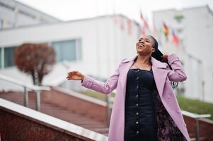 Jonge, stijlvolle, mooie afro-amerikaanse vrouw in straat met een mode-outfitjas tegen vlaggen van verschillende landen van de wereld