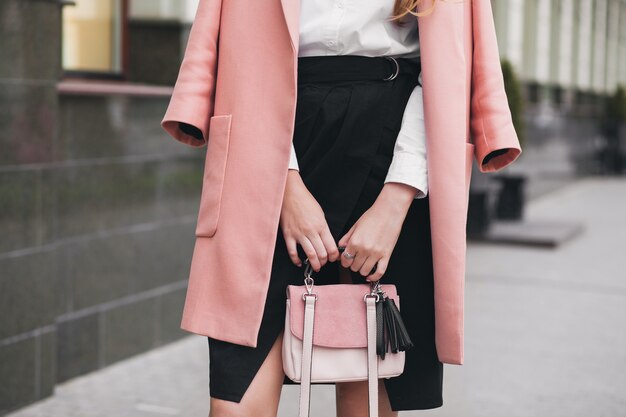 Jonge stijlvolle mooie vrouw die op straat loopt, roze jas draagt, handtas, zwarte rok, mode-outfit, herfsttrend, accessoires, handen close-up, details