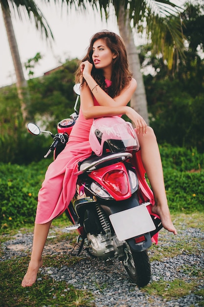 Jonge stijlvolle sexy mooie vrouw in roze jurk op scooter motor