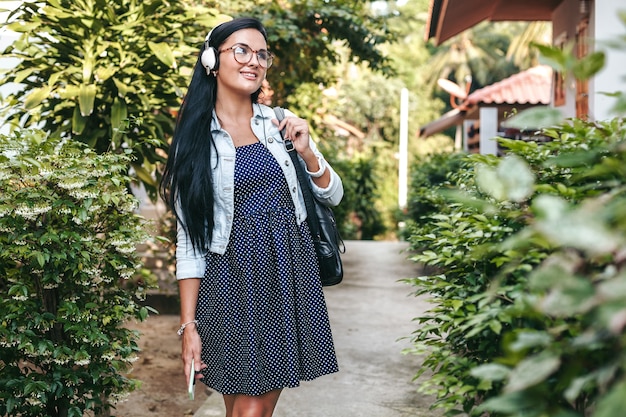 Jonge stijlvolle vrouw lopen met smartphone, luisteren naar muziek op de koptelefoon, zomervakantie