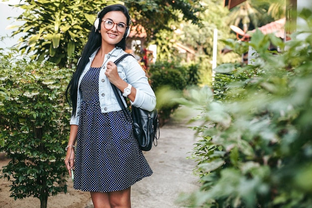 Jonge stijlvolle vrouw lopen met smartphone, luisteren naar muziek op de koptelefoon, zomervakantie