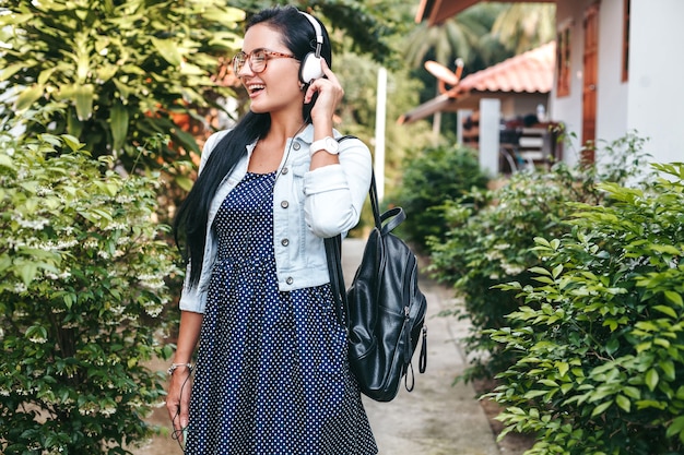 Jonge stijlvolle vrouw lopen met smartphone, luisteren naar muziek op de koptelefoon, zomervakantie