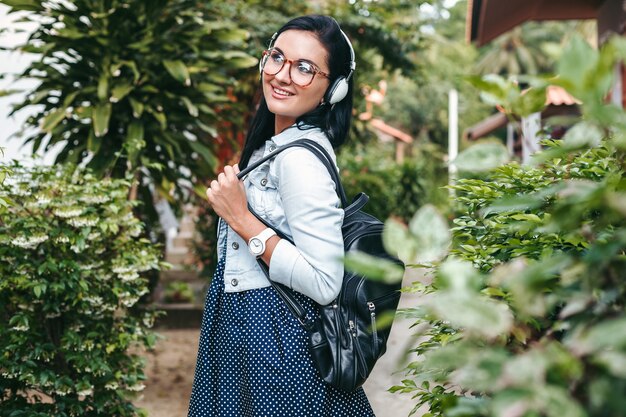 Jonge stijlvolle vrouw lopen met smartphone, luisteren naar muziek op de koptelefoon, zomervakantie