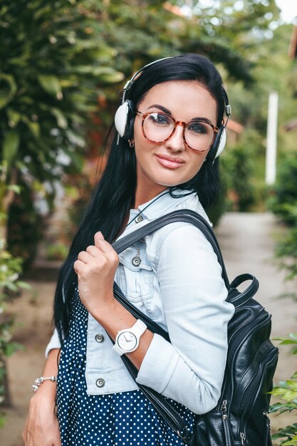 Jonge stijlvolle vrouw lopen met smartphone, luisteren naar muziek op de koptelefoon, zomervakantie