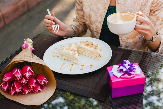 Jonge stijlvolle vrouw zitten in café, kopje cappuccino houden en lekkere taart eten,