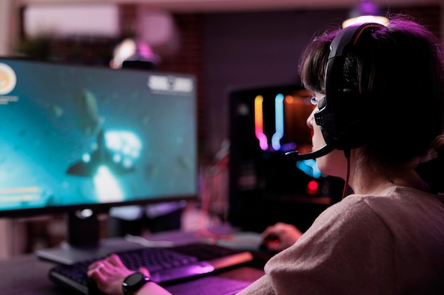 Jonge streamer die videogames online speelt op livestream, met behulp van computer en neonlichten in de woonkamer. Vrouwelijke gamer die plezier heeft met actiegameplay op virtueel schiettoernooi.