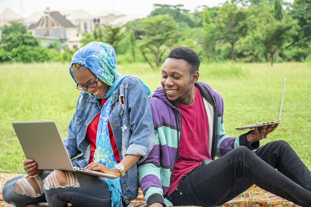 Jonge studenten zitten in een park en werken samen op hun laptop aan een universiteitstaak