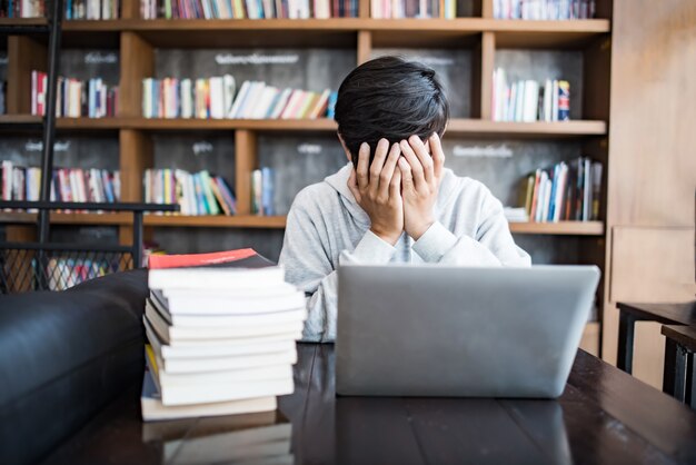 Jonge studentenmens die van computerzitting bij koffielijst wordt vermoeid met laptop