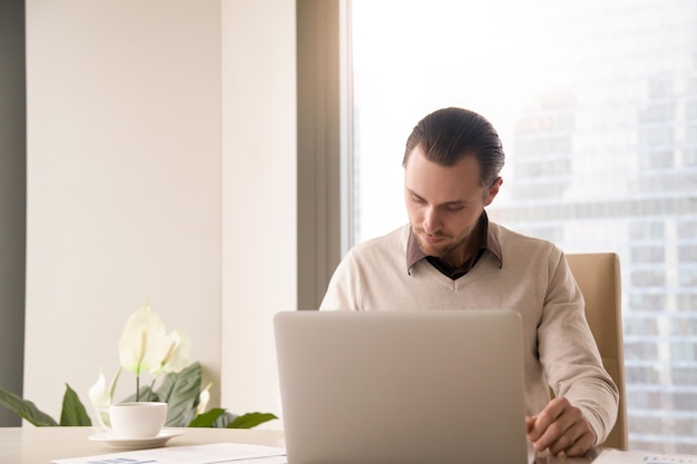 Jonge succesvolle zakenman die bij bureau werkt die laptop computer met behulp van