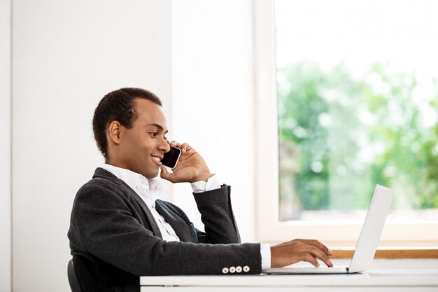 Jonge succesvolle zakenman die op telefoon spreekt, die laptop typt