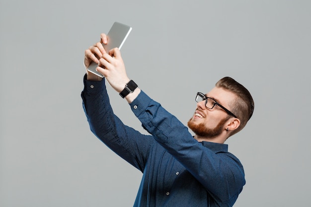 Jonge succesvolle zakenman die tablet over grijze muur bekijkt.