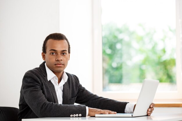 Jonge succesvolle zakenmanzitting op werkplaats met laptop