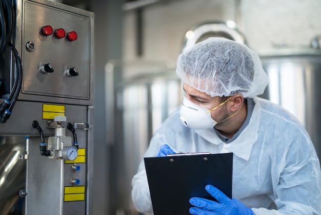 Gratis foto jonge technoloog in witte beschermende uniforme controle van industriële machine in productie-installatie