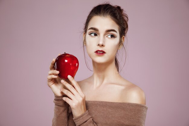 Jonge tedere vrouw die rode appel op roze houdt