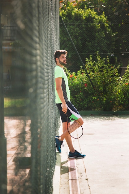 Jonge tennisspeler leunend tegen hek