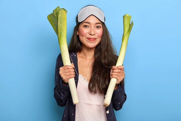 Jonge tevreden Koreaanse vrouw houdt verse rauwe geur vast, draagt een slaapmasker en nachtkleding en gaat een voedzame vegetarische salade maken