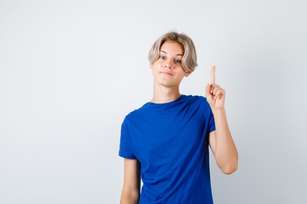 Jonge tienerjongen die omhoog wijst in een blauw t-shirt en er zelfverzekerd uitziet, vooraanzicht.