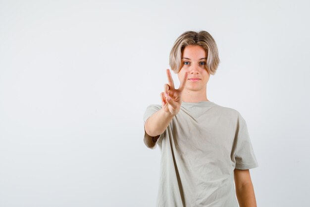 Jonge tienerjongen die vredesgebaar in t-shirt toont en vrolijk kijkt. vooraanzicht.