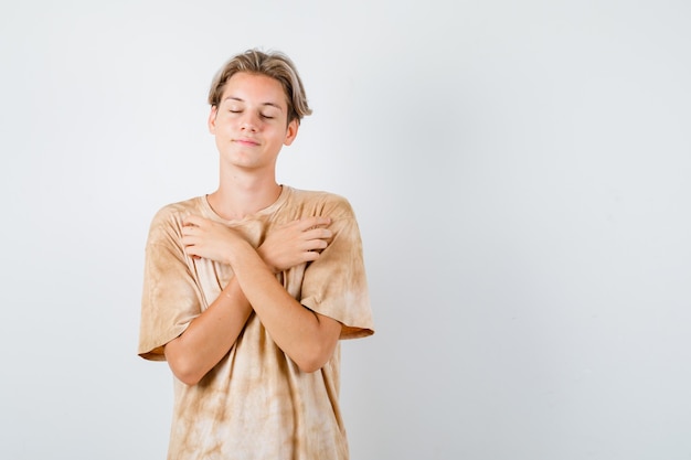 Jonge tienerjongen houdt gekruiste armen op de borst, sluit de ogen in een t-shirt en ziet er vredig uit. vooraanzicht.