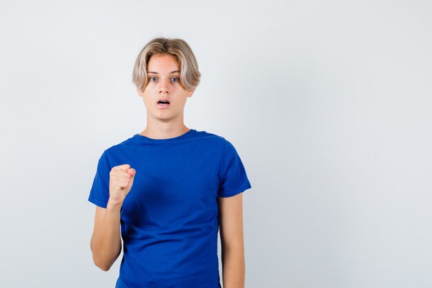 Jonge tienerjongen in blauw t-shirt met gebalde vuist en verbaasd, vooraanzicht.