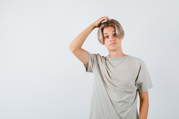 Jonge tienerjongen in t-shirt die aan zijn hoofd krabt en verbaasd kijkt